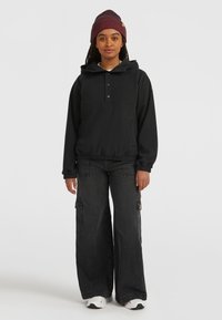 Black hooded sweatshirt with a buttoned front, paired with wide-leg dark denim cargo pants featuring side pockets. White sneakers and a burgundy beanie.