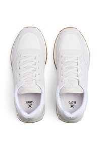 White sneakers with a leather and suede upper, flat laces, padded collar, and light brown rubber sole. Features logo on tongue.