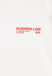 Tissu blanc avec un texte rouge indiquant "RUNNING LOW ON ENERGY, HIGH ON GOALS" et deux petits symboles de cœur à droite du texte.