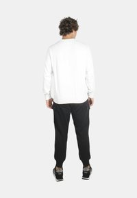 Camicia bianca a maniche lunghe con scollatura rotonda, abbinata a pantaloni cargo neri con tasche laterali. Scarpe da ginnastica nere completano il look.