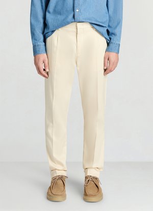 Pantalon beige clair à la texture lisse et devant plissé, associé à une chemise en denim bleu. Porté avec des chaussures en daim marron.