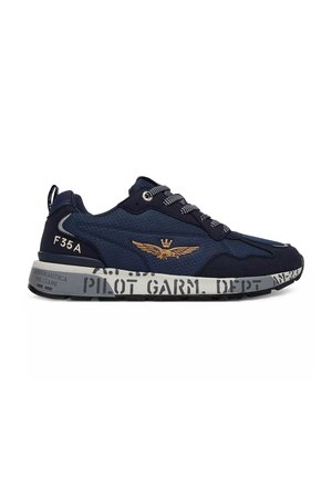 Sneaker blu navy con lacci neri e bianchi, emblema dorato alato sul lato, suola grigia con scritte e segni neri in stile militare.