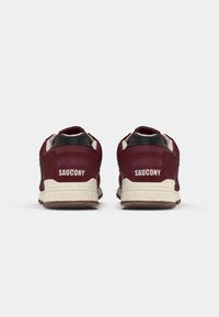 Burgunderfargede semskede sneakers med hvit logo på hælen, sorte detaljer og en strukturert gummisåle. Minimalistisk design med snøresystem.