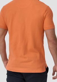 Oranje poloshirt met korte mouwen van katoen, met een rechte snit en zijsplitten aan de onderkant voor extra bewegingsvrijheid.