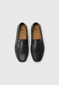 Pantofi slip-on din piele neagră, cu un finisaj texturat, având o talpă flexibilă și cusături contrastante. Logo-ul brandului este vizibil pe interior.