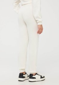 Białe spodnie dresowe z materiału sweatshirtowego, o zwężanym kroju, z elastycznym pasem i mankietami. Połączone z czarno-białymi butami sportowymi.