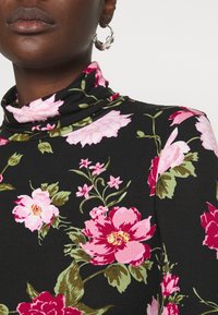 Svart blommig tubhals med stora rosa och gröna blommor. Mjuk tyg med en slät yta och en åtsittande design som visar intrikata detaljer.