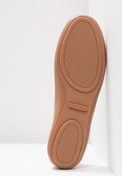 Beige Leder-Ballerina mit einer strukturierten Gummisohle, die ein geometrisches Muster aufweist. Auch seitliche Markenkennzeichnung ist sichtbar.