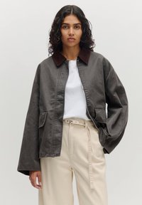 Grijze jas met een bruine ribgebreide kraag, zachte stof, voorzakken en een ontspannen pasvorm, gecombineerd met een wit shirt en beige broek.