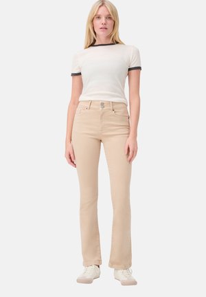 Beige Schlagjeans mit hoher Taille, zwei Fronttaschen und silberne Knopfverschluss, kombiniert mit einem weißen T-Shirt mit schwarzem Saum.