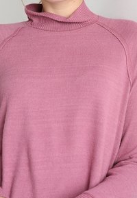 Rosafarbener, weicher Strickrollkragenpullover mit geripptem Kragen und Raglanärmeln. Die Textur wirkt glatt mit feinen Farbvariationen.
