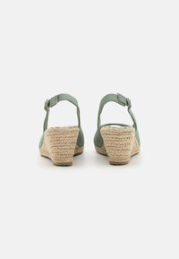 Sandales compensées en toile verte avec un talon en jute tressé. Bride de cheville ajustable avec une boucle en métal. Design ouvert à l'arrière.