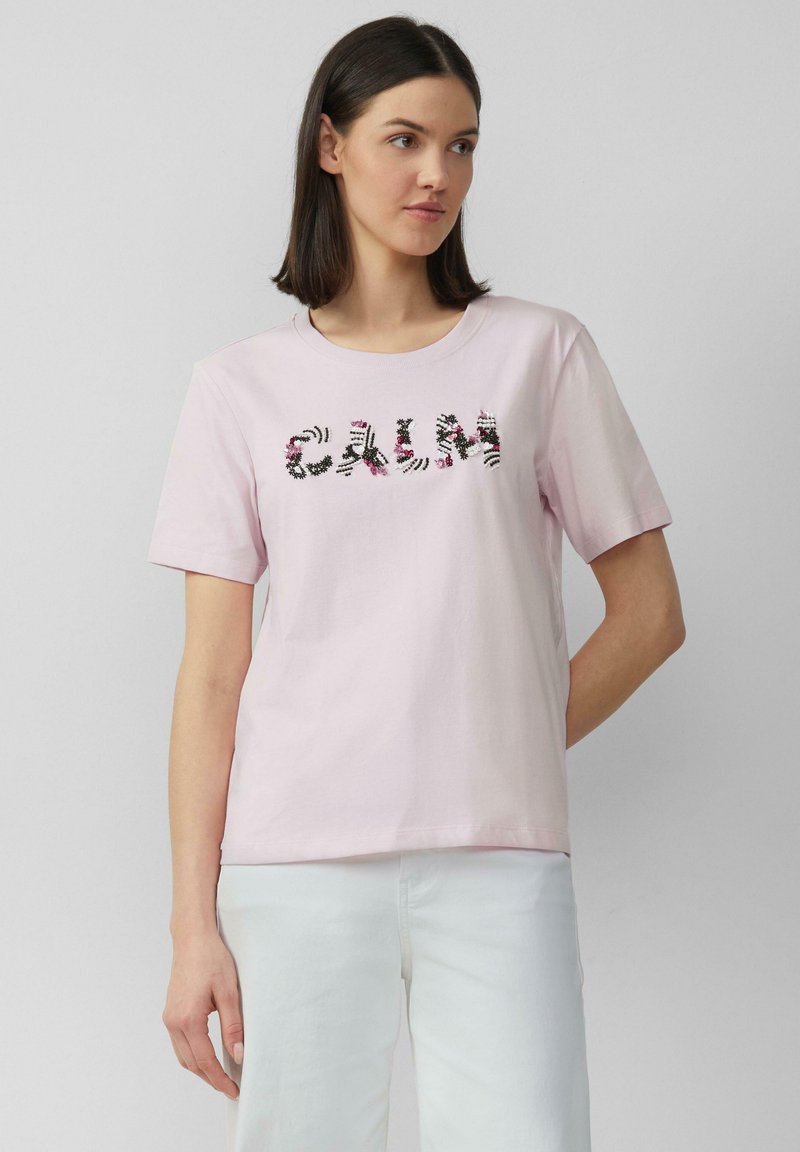 T-shirt en coton rose à manches courtes, arborant le mot "CALM" dans un motif noir et floral sur le devant.