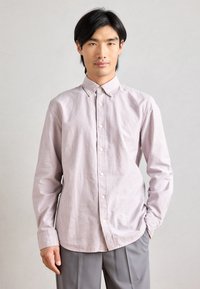 Ljust randig skjorta med knappar i lavendel och vitt, med klassisk krage och långa ärmar, tillsammans med grå byxor.