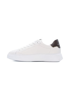 Sneaker bianco basso con chiusura frontale con lacci e linguetta nera sul tallone su una suola bianca grossa, vista dal lato interno su sfondo bianco.