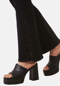 Los jeans negros acampanados presentan aberturas laterales con acentos trenzados. Combinados con sandalias de plataforma negras, que muestran un diseño de punta con corte.