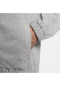 Material de sudadera gris con puños acanalados y un bolsillo lateral. La textura parece suave y ligeramente peluda, adecuada para un estilo casual.