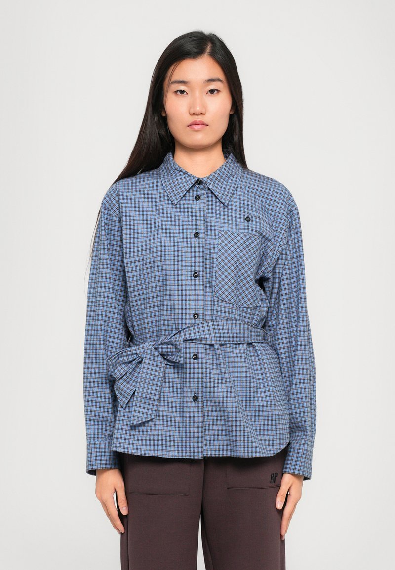 Sinine ja must ruuduline särk kraega, nööbiga kinnitusega, eestaskuga ja seotud vöökohaga. Pehme kangas struktureeritud sobitusega.