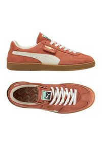 Sneakers Puma in suede color ruggine con accenti bianchi. Presentano una linguetta imbottita, lacci bianchi e una suola di gomma marrone. Logo sulla linguetta.