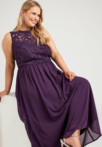 Violetti maksimekko, jossa on pitsikroppa kukkakuoseilla, virtaava hame ja joustava vyötärö. Korostettu hopeisilla koristeilla.