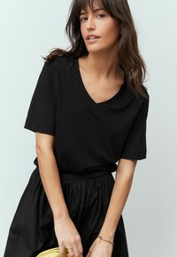 Zwarte katoenen t-shirt met een v-hals, korte mouwen en een relaxte pasvorm, gecombineerd met een zwarte rok en een gele clutch bag.