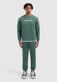 Groen sweatshirt en bijpassende joggers met een witte "BALLIN'" opdruk. Het sweatshirt heeft een ronde hals; de joggers hebben een elastische tailleband en zijzakken.