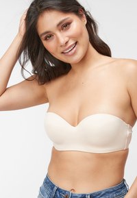 Reggiseno beige senza spalline con coppe lisce e sagomate e una cucitura centrale decorativa, abbinato a pantaloni shorts in denim.