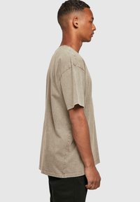 Lys beige kortermet t-skjorte i avslappet passform, med rund halslinje og synlige sømdetaljer. Stoffet ser mykt og teksturert ut.