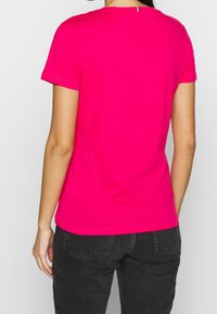 Camiseta de algodón ajustada rosa con mangas cortas y cuello redondo. Textura suave, diseño simple, sin patrones ni detalles de hardware.