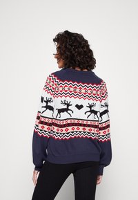 Marinblå stickad tröja med ett festligt mönster, som har röda och vita zigzag-mönster samt svarta renar, långa ärmar och ribbad fåll.
