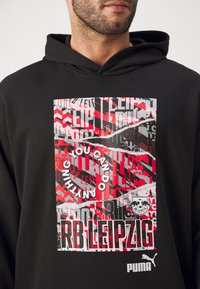 Sort hættetrøje med et grafisk tryk i rød, hvid og grå med forskellige tekstelementer, herunder "RB Leipzig" og et logo.