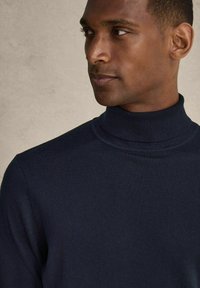 Mörkblå polotröja gjord av ett mjukt stickat tyg. Har en tät passform med ribbad krage och manschetter.