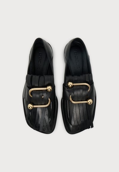 Paire de mocassins en cuir noir avec détail à franges et boucle dorée incurvée sur le dessus, vue de dessus sur fond blanc.
