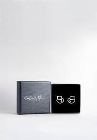 Silvriga kattformade örhängen visas upp på en svart sammetbakgrund inuti en texturerad svart smyckeslåda märkt "Sofia Milani Jewels."
