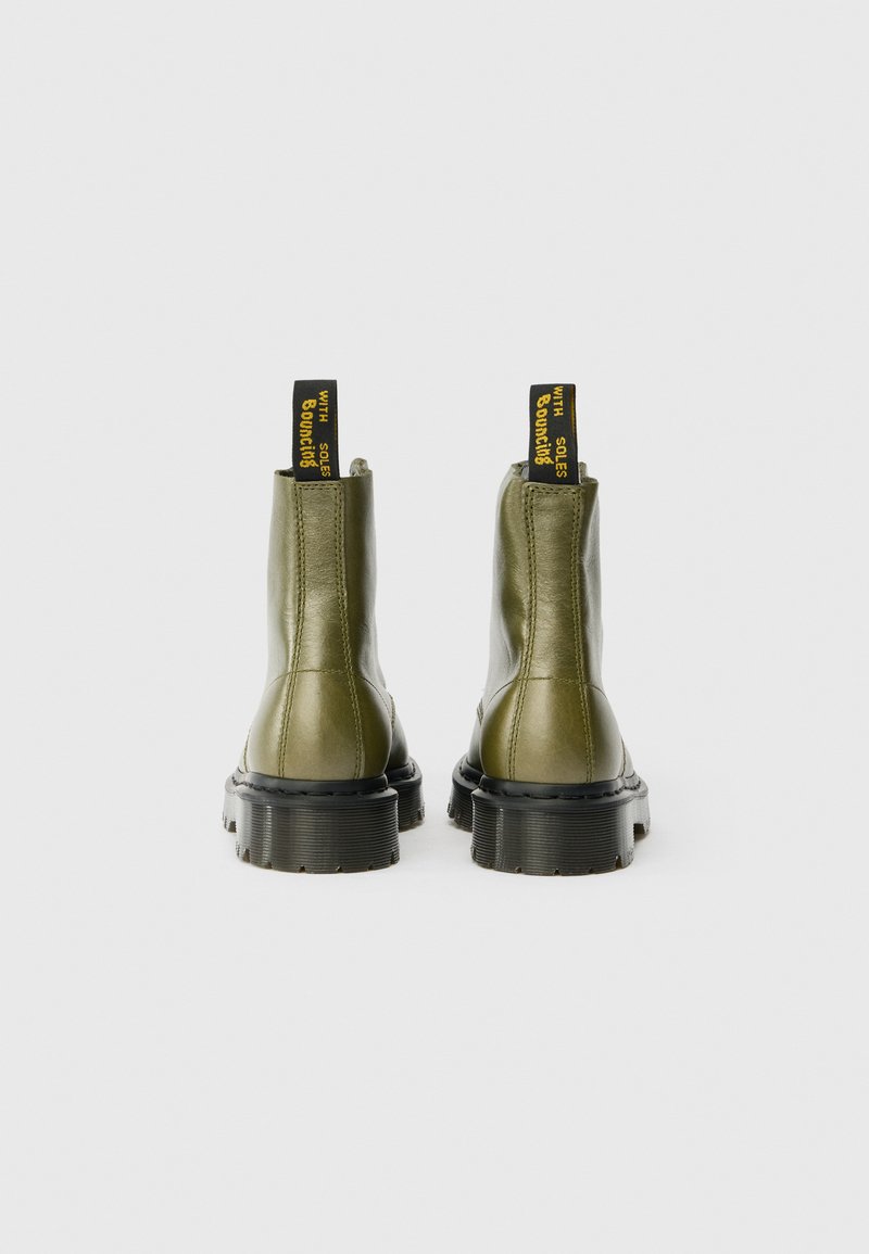 Olivgrüne Lederstiefeletten mit schwarzen, derben Sohlen, ausgestattet mit gelben Schlaufen an der Rückseite und glatter Textur.