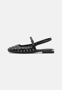 Crna slingback cipela od kože, s metalnim šiljcima na gornjem dijelu, ravnim potplatom i podesivim remenom za prilagodbu i udobnost.