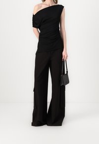 Czarna bluzka bez ramiączek z marszczonym detalem, połączona z szerokimi czarnymi spodniami z bocznymi kieszeniami i małą czarną torebką.