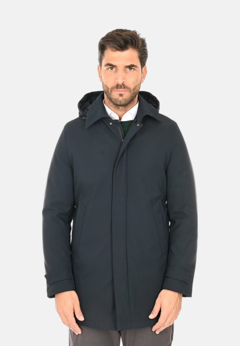 Parka impermeabile blu navy con cappuccio removibile, zip frontale, due tasche laterali e una texture liscia. Presenta un taglio sartoriale e cuciture discrete.