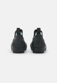 Black rubber ankle boots with textured surface, mint green accents, rear pull tabs, and logo detail on heel. Designed for comfort and support.