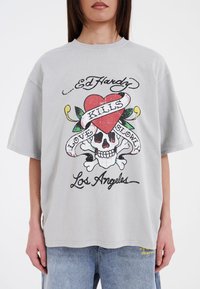 Grijze oversized t-shirt met een grafisch ontwerp van een hart, schedel en tekst in rood en zwart. Gemaakt van katoen met een ronde hals.