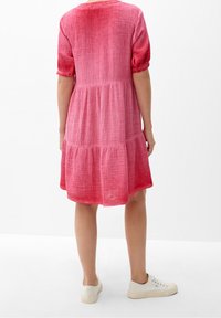 Robe en coton rose avec des manches courtes, tissu texturé, design à volants, longueur genou, assortie à des baskets blanches.