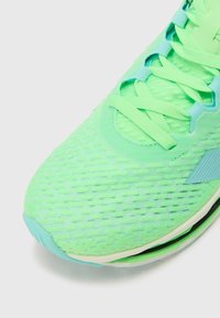 Green running shoe featuring a textured mesh upper, flat laces, and a cushioned sole with a slight curve at the toe and aqua accents.