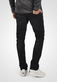 Jeans de mezclilla negros con corte ajustado, bolsillos traseros y un suéter gris texturizado. Combinados con zapatillas blancas que presentan sutiles colores de acento.