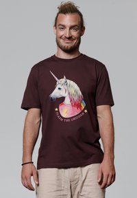 Bordeauxrotes Baumwoll-T-Shirt mit einem Einhorn-Grafikdesign, das eine Regenbogenmähne und einen Blitz zeigt. Der Text enthält "FLASH THE UNICORN" in einem kreisförmigen Design.