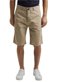 Beżowe bawełniane spodenki o prostym kroju z bocznymi kieszeniami, z zapięciem na guzik i szlufkami na pasek. Noszone z białymi sneakersami.