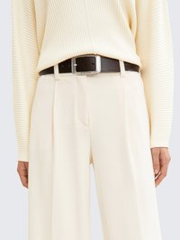 Haut à longues manches côtelé crème associé à un pantalon large taille haute beige clair, maintenu par une ceinture noire avec une boucle en argent.