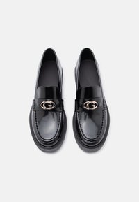 Juodos blizgios loafers tipo bateliai su apvaliu pasirinkimu, maža aukso emblemą ant dirželio ir tekstūruota siuvimo linija palei kraštą. Lygus vidinis apdorojimas.