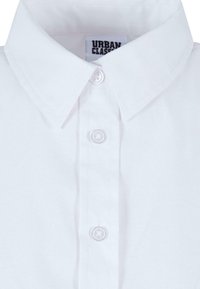 White collared shirt with a buttoned placket, made of smooth fabric. Features a tag labeled "URBAN CLASSIC" at the collar.