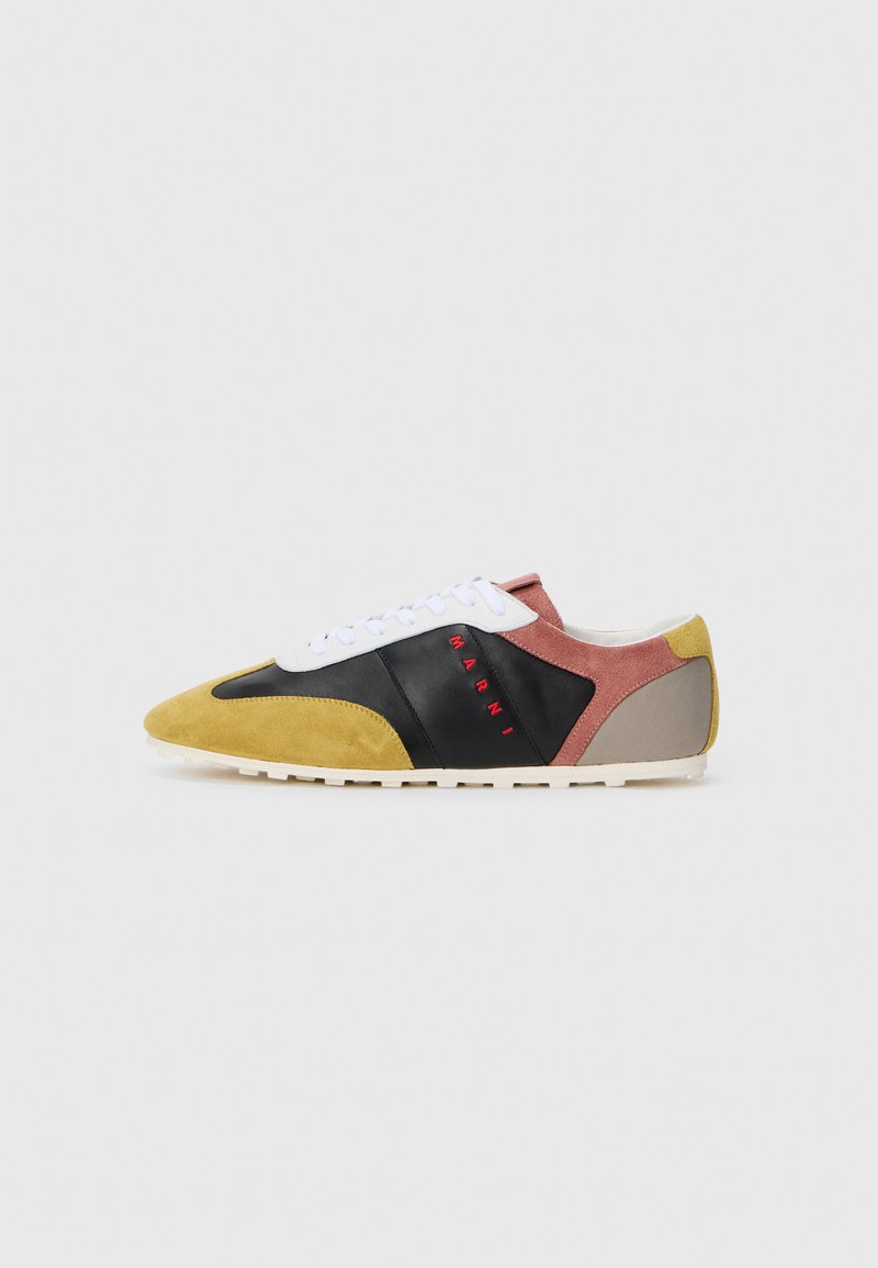 Sneaker multicolore con punta in suede gialla, corpo in pelle nera, dettagli rosa e grigi. Lacci bianchi e logo rosso sul lato.
