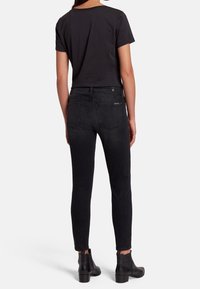 Black fitted jeans with a smooth texture, five pockets, and subtle stitching details, paired with a short-sleeved black t-shirt and black ankle boots.